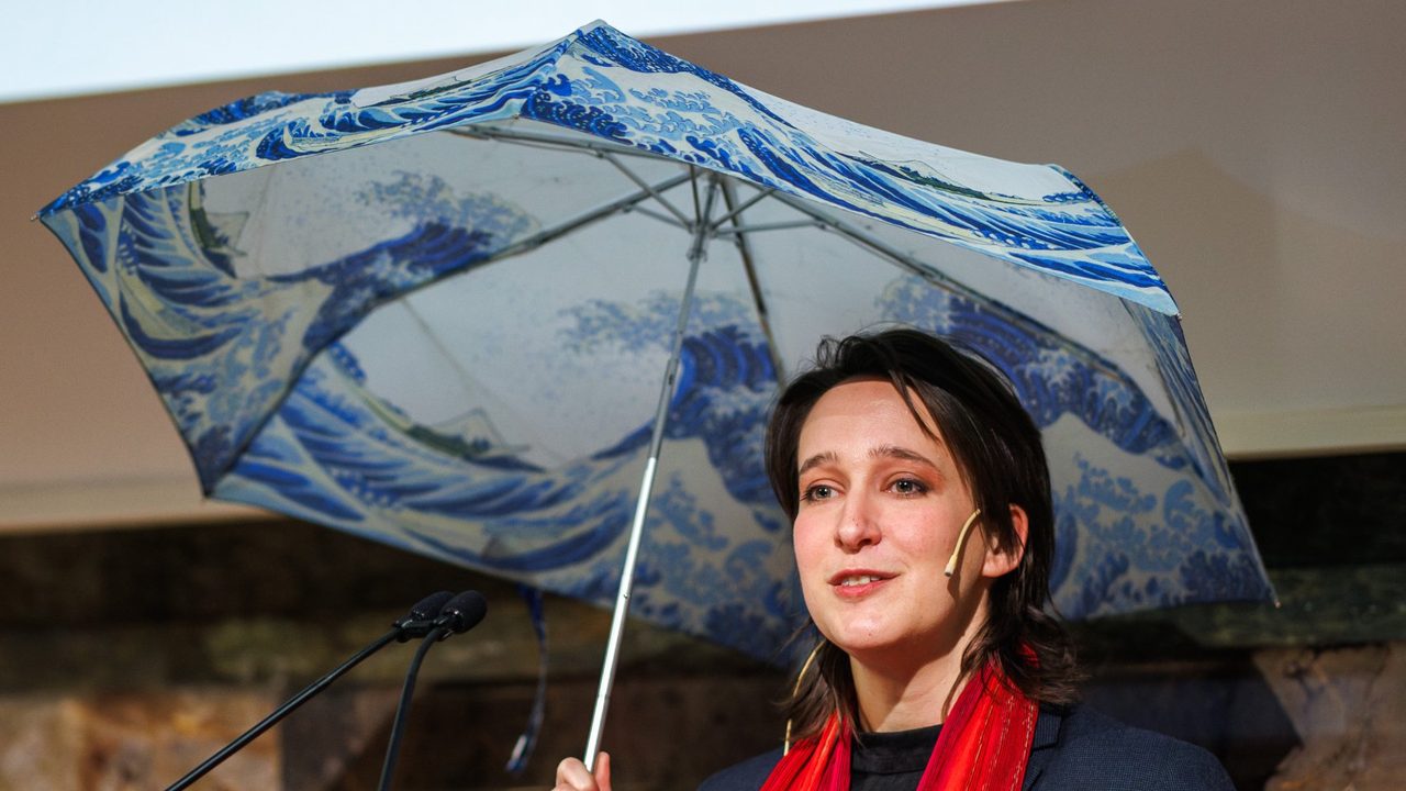 Stephanie Santschi speaking at the University of Zurich, holding an umbrella printed with Hokusai’s Great Wave